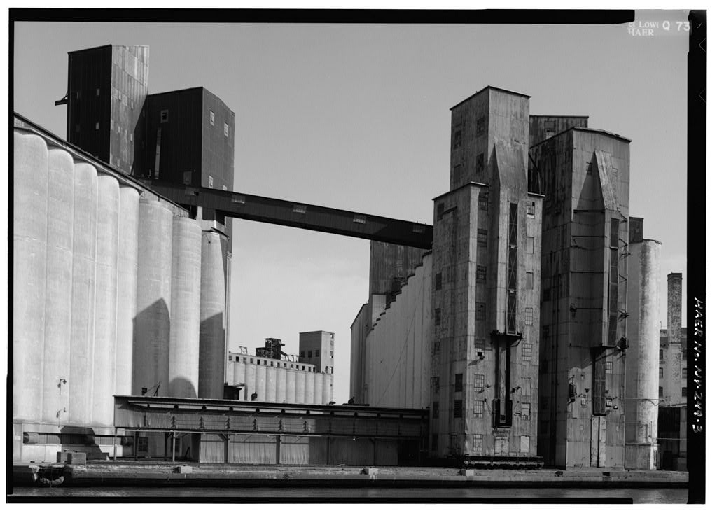 NY-249-5 American Elevator looking East, barely visible behind American Malt House with Russell-Miller Flour Mill to right (Now Eonacara and idle). Jet Lowe, Photographer, 1985.